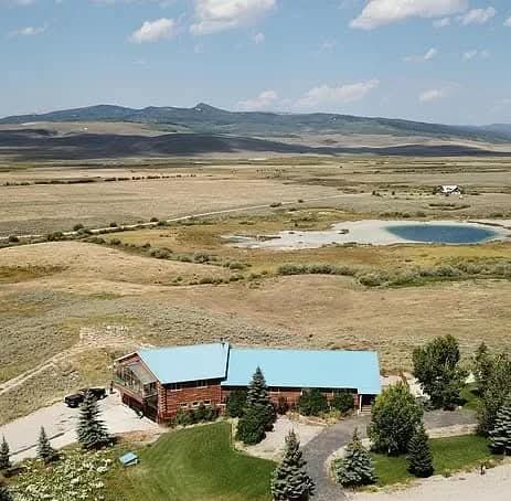 Aerial view of the cattery's log home set against the mountains and prairie pond